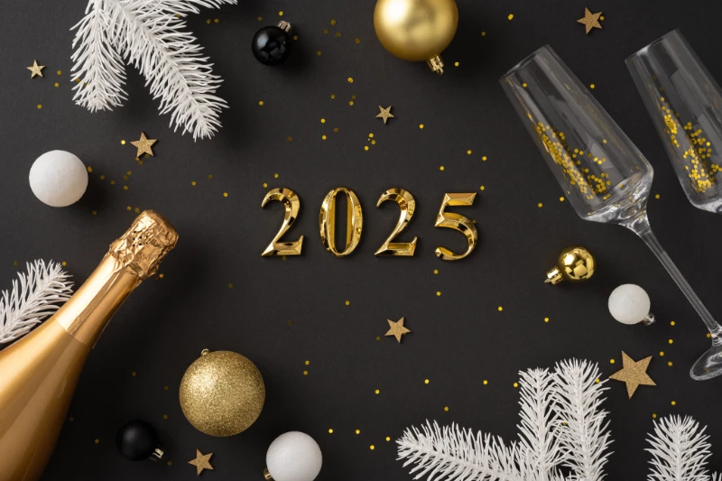 Gold balloons forming 2025 surrounded by champagne bottle, glasses, white pine branches, gold and black ornaments, and confetti on a dark background, creating a festive New Year’s celebration scene.